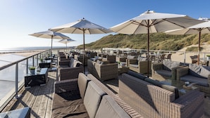 Un bar en la azotea con mobiliario de mimbre, sombrillas exteriores y vistas a la playa.