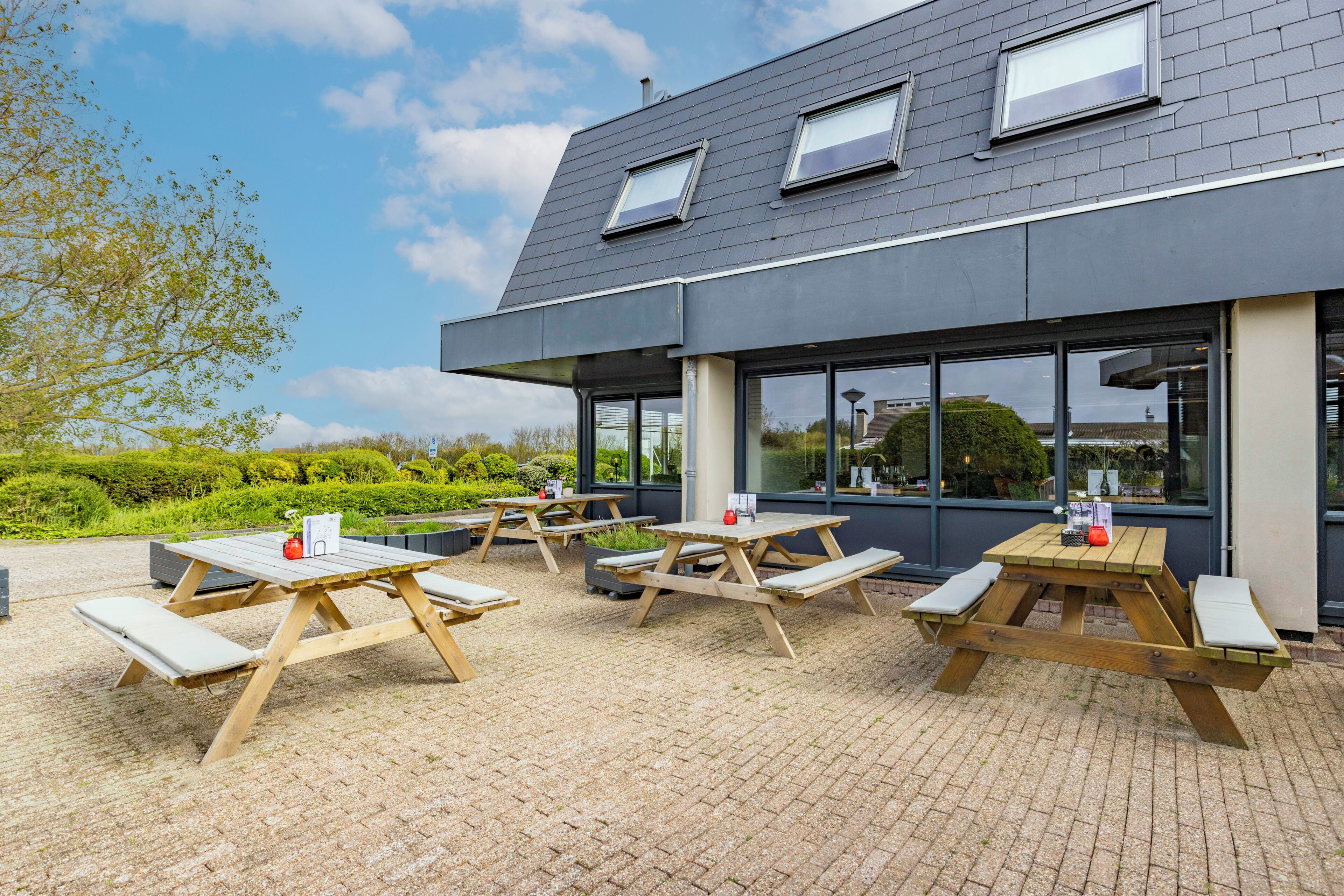 Un espace extérieur aménagé en terrasse, avec des tables de pique-nique, et un bâtiment doté de grandes fenêtres.