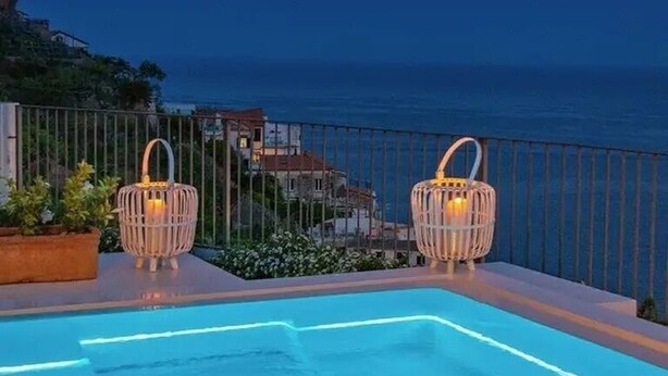 A swimming pool with two wicker lanterns and a view of the sea at dusk. - Villa Domi by My Villa Collection (Amalfi)