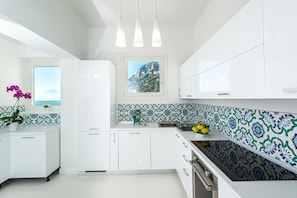 A modern kitchen with white cabinets, a tiled backsplash, and a window with a coastal view. - Villa Domi by My Villa Collection (Amalfi)