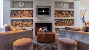 Ein modernes Wohnzimmer mit Kamin, Sofas und einem darüber montierten Fernseher.