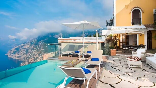A rooftop infinity pool with lounge chairs and umbrellas, overlooking a mountainous coastline. - Villa Deus by My Villa Collection (Nocelle)