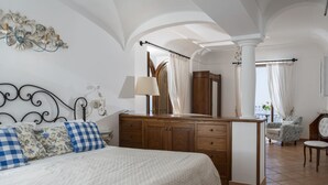 A bedroom with a large bed, wooden dresser, and a sitting area with a chair and table. - Villa Deus by My Villa Collection (Nocelle)