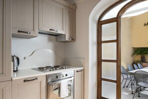 A kitchen with wooden cabinets, a stainless steel stove, and a view of an outdoor patio with chairs and a table. - Villa Deus by My Villa Collection (Nocelle)