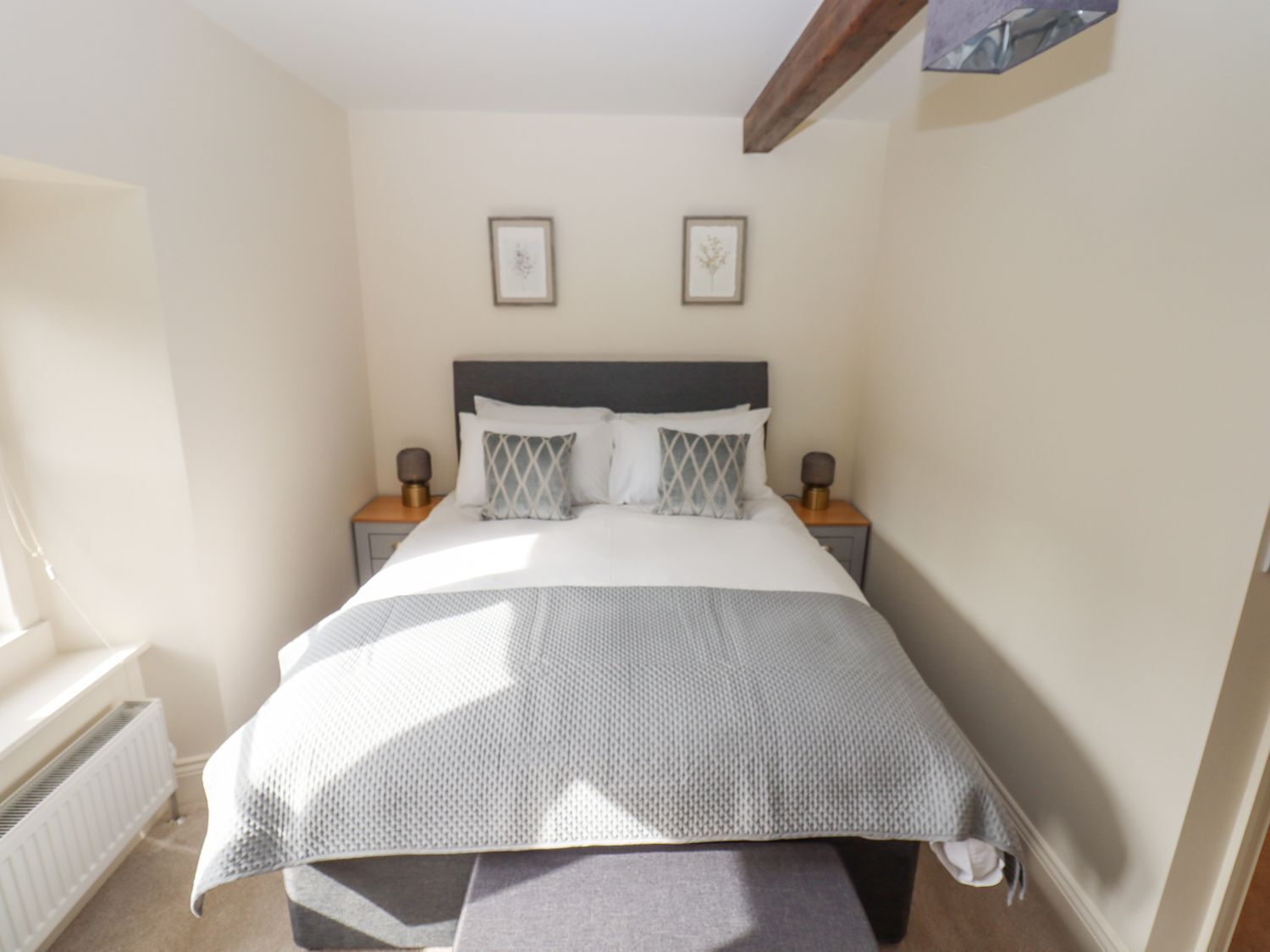 A bedroom with a bed, two bedside tables, a radiator, and two framed pictures on the wall.