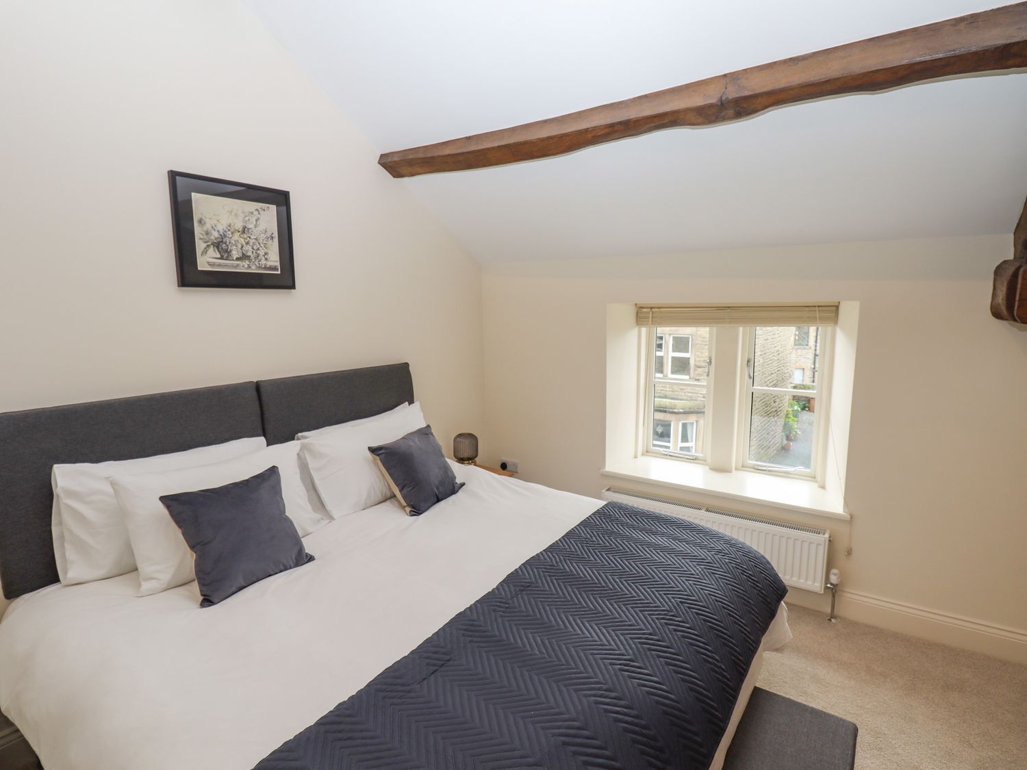 A bedroom with a bed, a framed picture on the wall, a window with a view, and a radiator.
