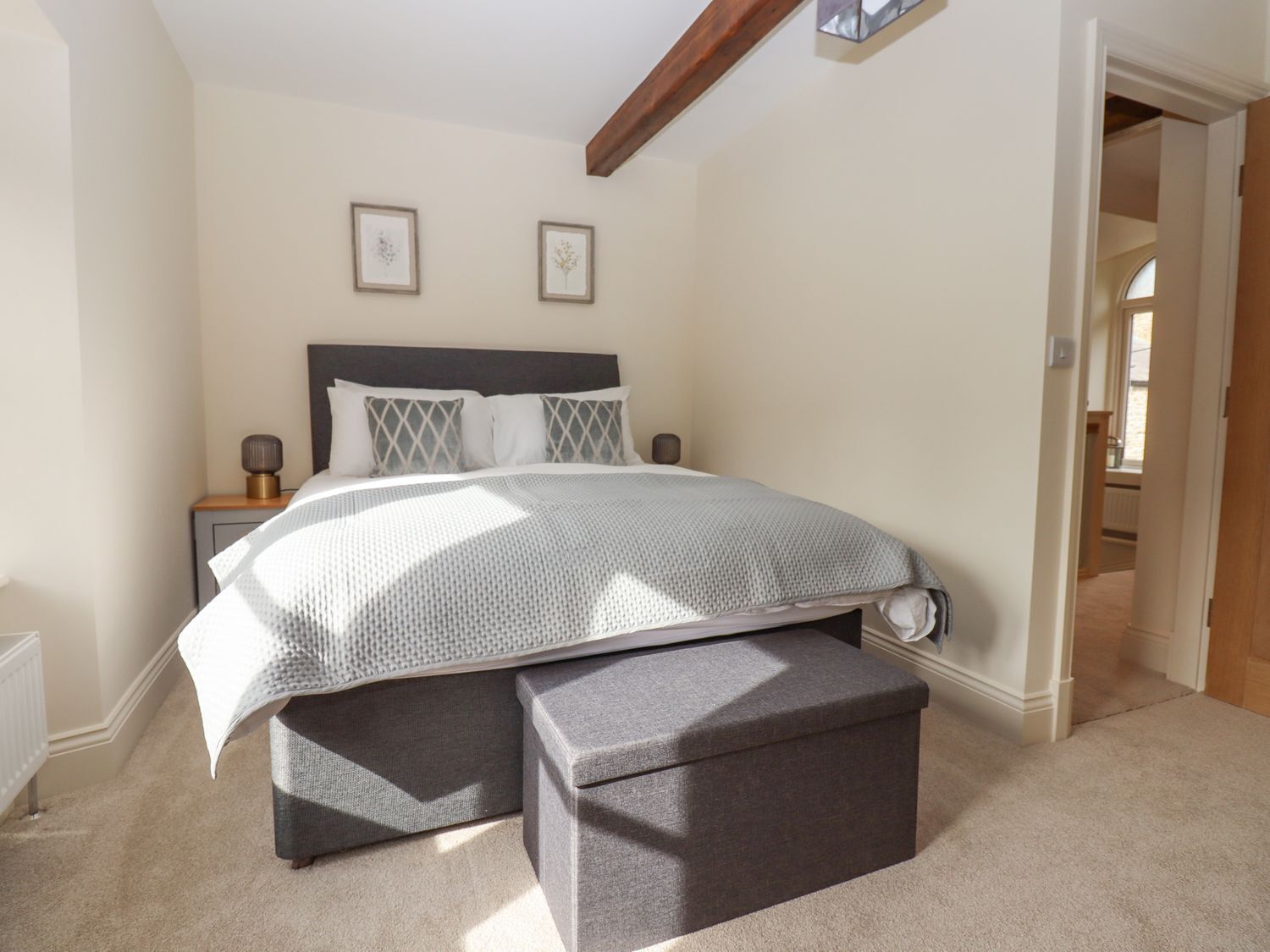 A bedroom with a bed, bedside tables, a nightstand, a bench, and framed pictures on the wall.