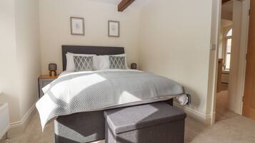 A bedroom with a bed, bedside tables, a nightstand, a bench, and framed pictures on the wall.