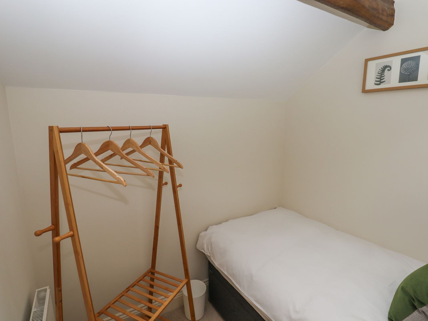A bedroom with a wooden drying rack, a single bed, and a framed picture on the wall.
