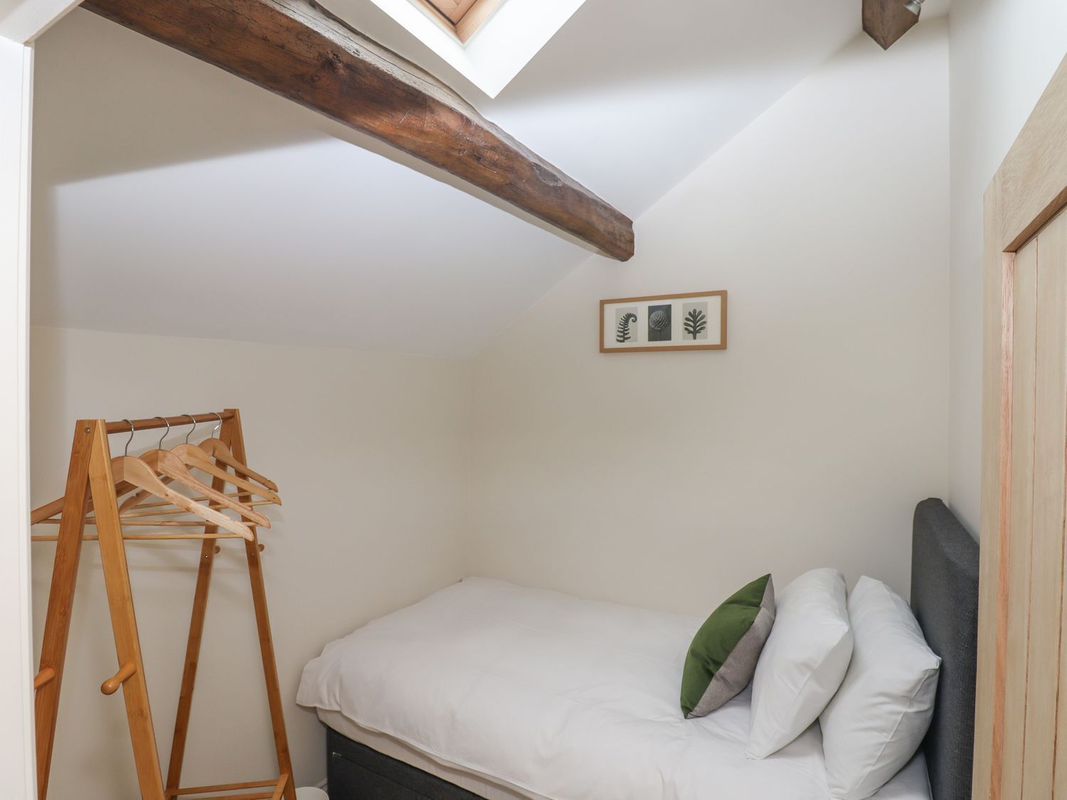 Un dormitorio con estructura de cama de madera, perchero de madera e impresión botánica enmarcada en la pared.
