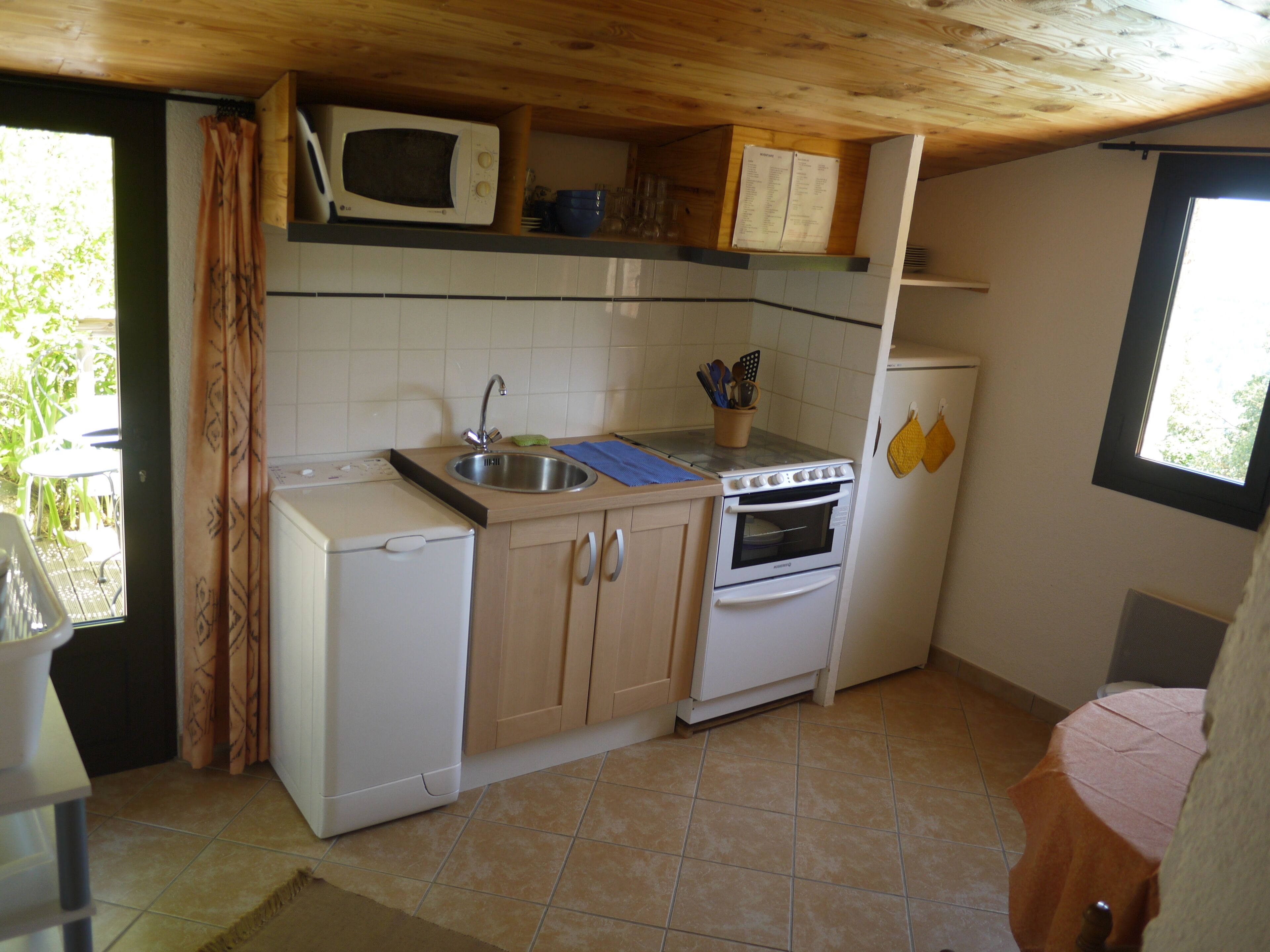 Una cocina compacta equipada con microondas, fregadero, horno y un refrigerador pequeño.