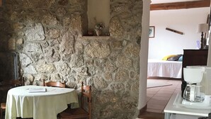 Una stanza con pareti in pietra, un tavolo da pranzo con sedie, un angolo cottura con lavello e un letto sullo sfondo.