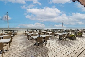 Een buiten eethoek met tafels en stoelen, met uitzicht op zee.