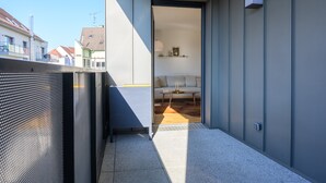 A modern balcony with a metal railing, a view of a residential area, and a glimpse into a room with a sofa and a table. - Colmar Chic – Modern Old Town Apartment with Wi-Fi, Garage, Elevator for 2–6 Guests (Colmar)