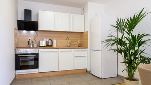 A modern kitchen with white cabinets, a black oven, a white refrigerator, and a potted plant. - Colmar Chic – Modern Old Town Apartment with Wi-Fi, Garage, Elevator for 2–6 Guests (Colmar)