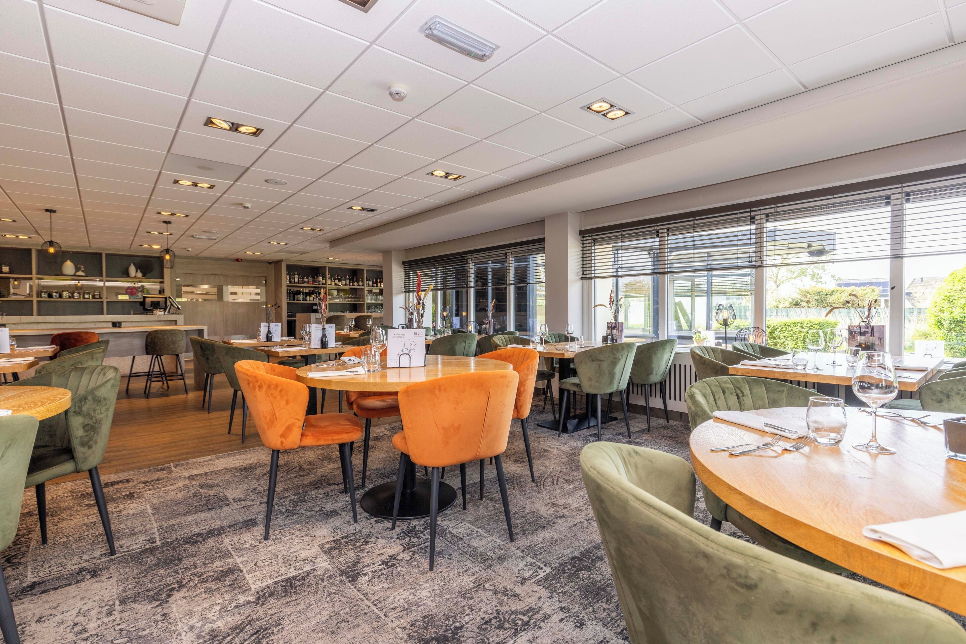 Un restaurant moderne avec des tables et des chaises rondes, un bar et de grandes fenêtres donnant sur l’extérieur.