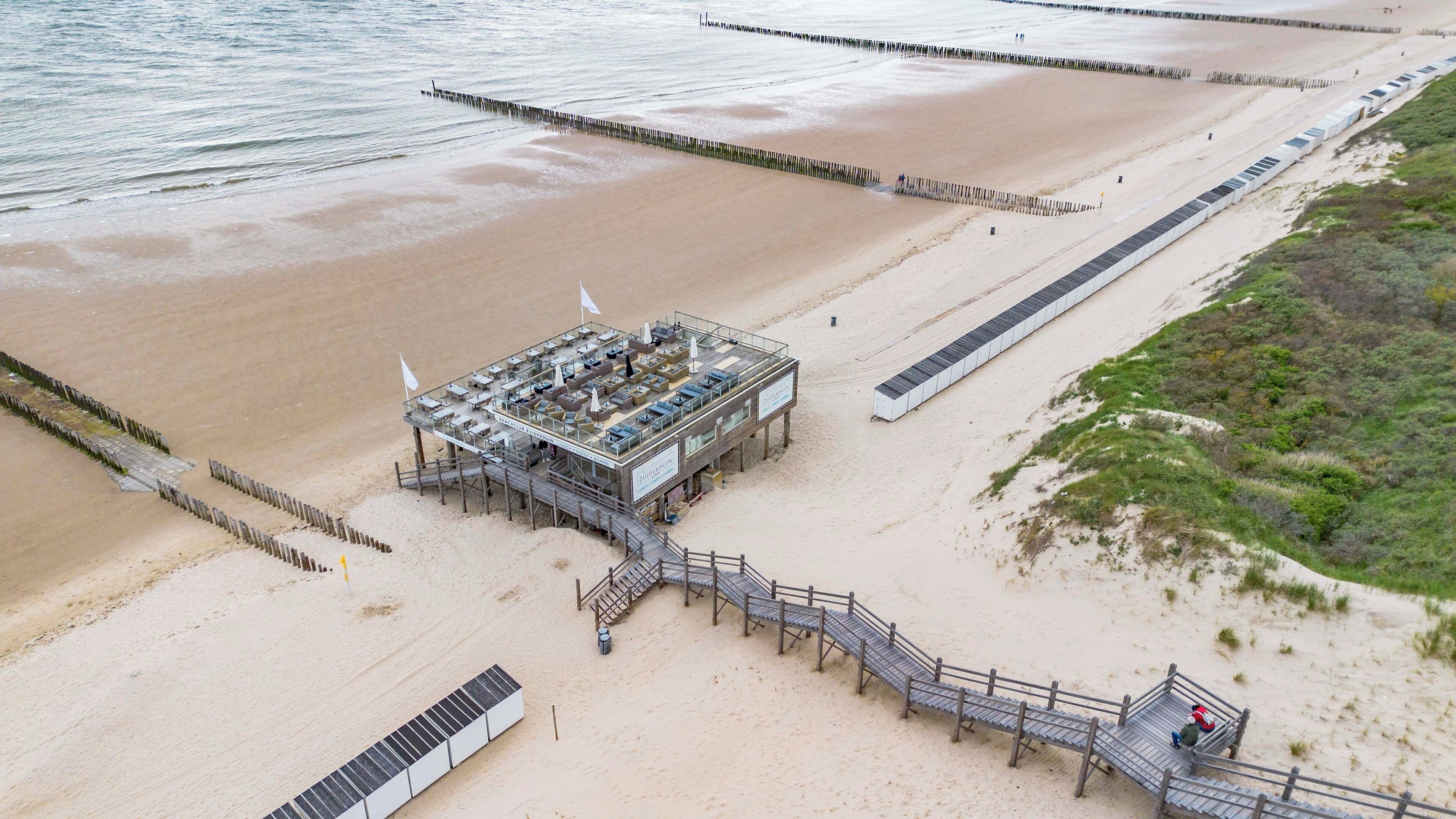 Ein Luftbild eines Strandhotels mit einem großen Gebäude, einer langen Pier und einem Weg zum Strand.