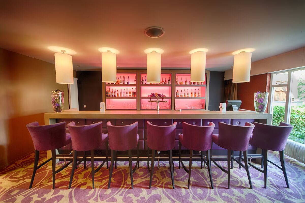 A bar area with purple bar stools, a long counter with bottles, and pendant lights.