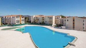 A swimming pool surrounded by multi-story buildings with balconies, under a clear sky. - Le Cosy du lagon Bleu (Fréjus)