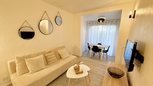 A living room with a sofa, a coffee table, a TV, and a dining area with chairs and a table. - Le Cosy du lagon Bleu (Fréjus)