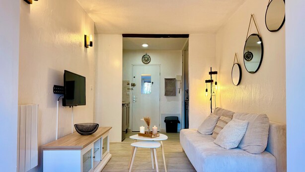 A modern living room with a sofa, a TV, a small table, and decorative wall lights. - Le Cosy du lagon Bleu (Fréjus)