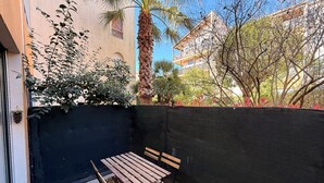 A patio with a table and chairs, a palm tree, and a building in the background. - Le Cosy du lagon Bleu (Fréjus)
