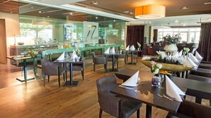 Un restaurante con una decoración moderna, que presenta suelos de madera, separadores de vidrio y diversas opciones de asientos, incluyendo mesas y sillas.