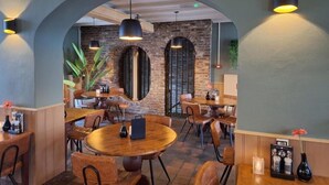 Un restaurante con mesas y sillas redondas, un muro de ladrillo y lámparas colgantes.