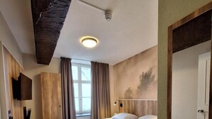 A hotel room with a large bed, a chair, a TV mounted on the wall, and a window with curtains. - Peaceful Stay in Thorn – Explore Cobblestone Streets, Historic Buildings (Thorn)