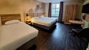 Een hotelkamer met twee bedden, een kleine tafel, een stoel, een televisie en een raam met gordijnen.