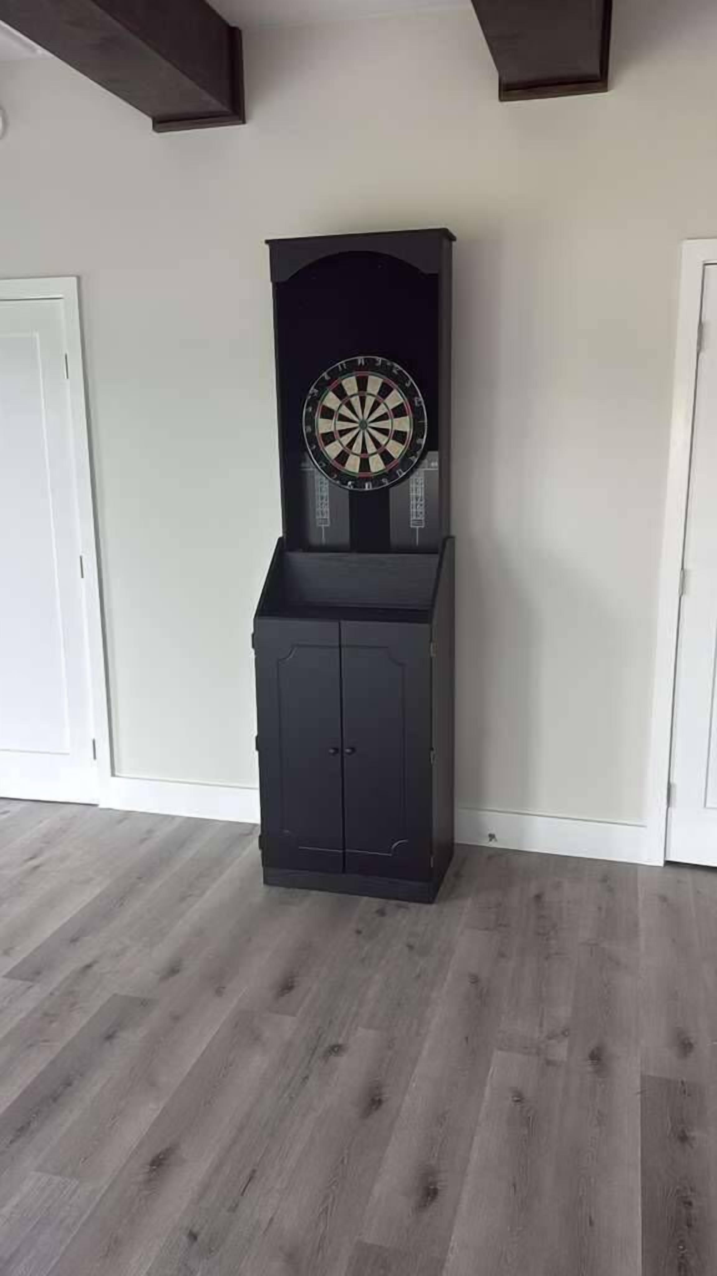 A room with a dartboard mounted on a wall above a black cabinet.