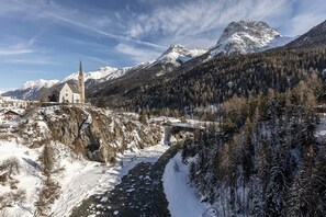 Eine Kirche mit einem hohen Turm, eine Brücke und verschneite Berge im Hintergrund.