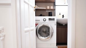 A compact laundry area with a front-loading washing machine, a shelf with toiletries, and a sink. - Design Micro-Studio - 10 minutes to Central Station (Vienna)