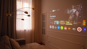 A living room with a large screen displaying a streaming service interface, a sofa, and a decorative light fixture. - Design Micro-Studio - 10 minutes to Central Station (Vienna)