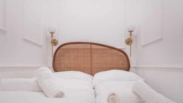 A neatly made bed with white linens and a woven headboard. - Design Micro-Studio - 10 minutes to Central Station (Vienna)