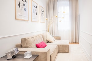 A modern living room with a beige sofa, a pink pillow, and a small table with a radio and a decorative item. - Design Micro-Studio - 10 minutes to Central Station (Vienna)