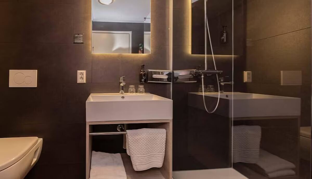 Une salle de bain moderne avec un grand miroir, un lavabo blanc et une douche séparée par des parois en verre.