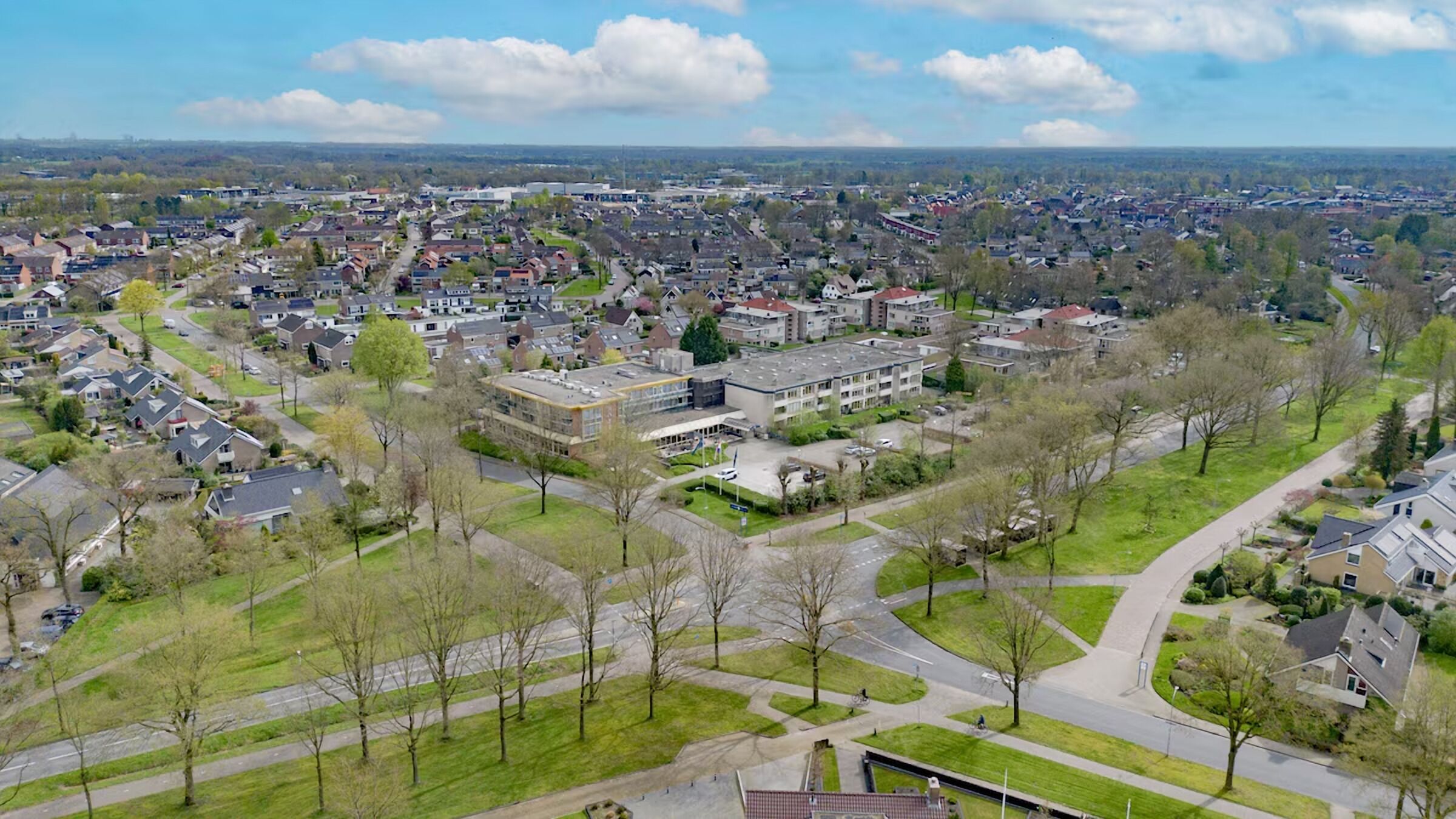 An aerial view of a residential area with a large building complex, surrounded by houses and green spaces.