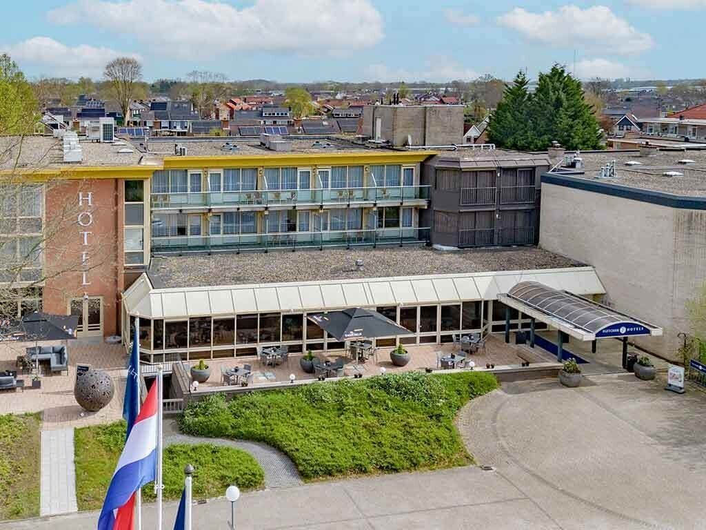 A hotel with a modern design, featuring a large glass facade, outdoor seating area, and a flagpole with flags.