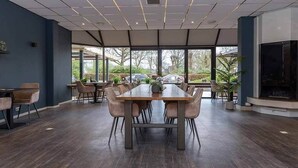 Un vaste espace dédié à la salle à manger, avec une longue table et des chaises, de grandes fenêtres offrant une vue sur l’extérieur et un design moderne au niveau du plafond.
