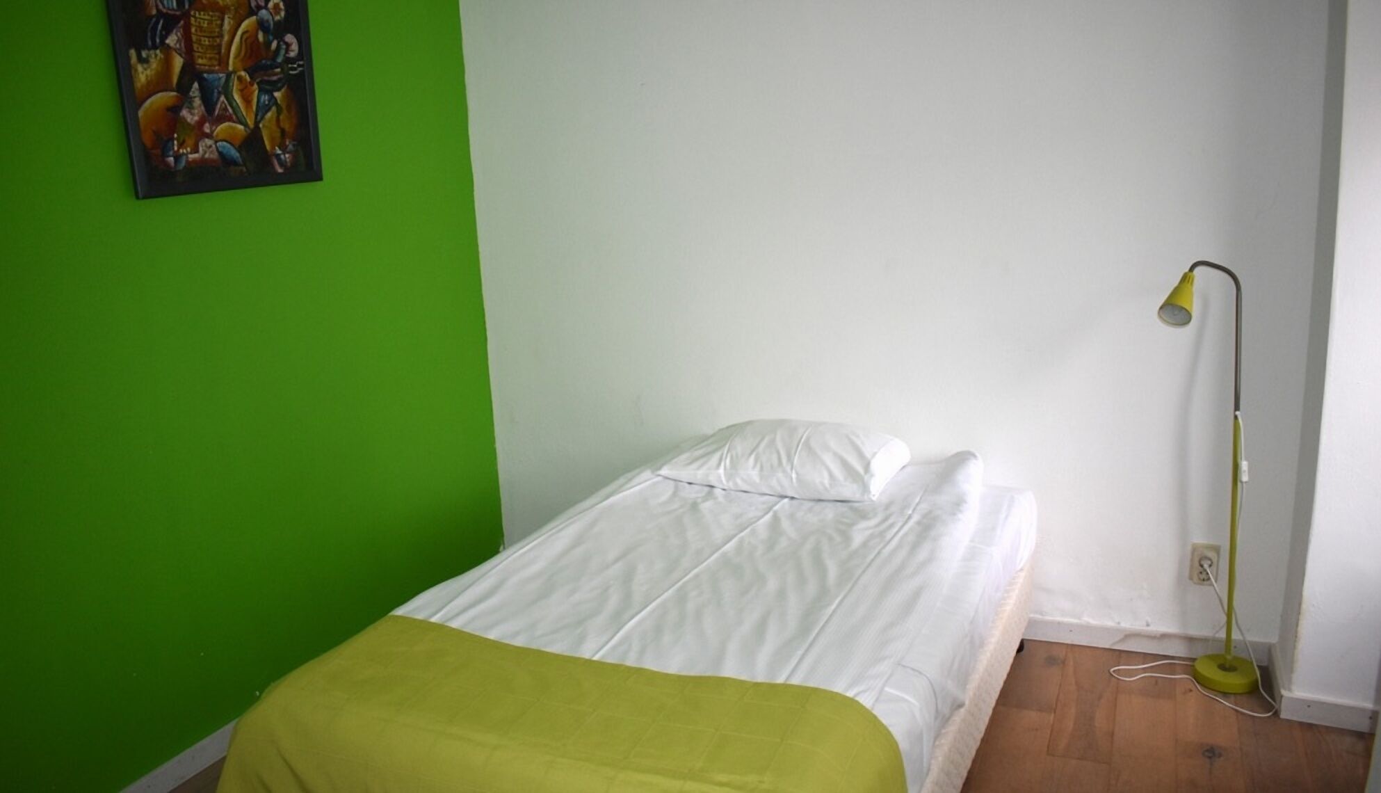 A small, single-bed room with a green wall and a white bedspread.