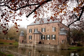 Ein historisches Backsteingebäude mit zahlreichen Fenstern und einem Turm, gelegen an einem ruhigen Gewässer.