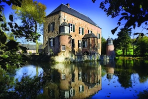 Ein historisches Gebäude mit einem Burggraben, das einen zentralen Turm und zahlreiche Fenster aufweist.
