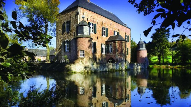 Een historisch gebouw met een gracht, met een centrale toren en meerdere ramen.