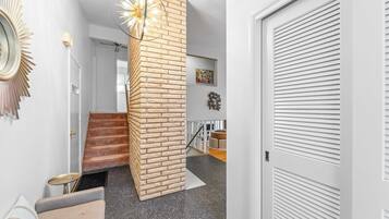 Uma escadaria com parede de destaque em tijolo, uma mesa redonda e uma luminária moderna.