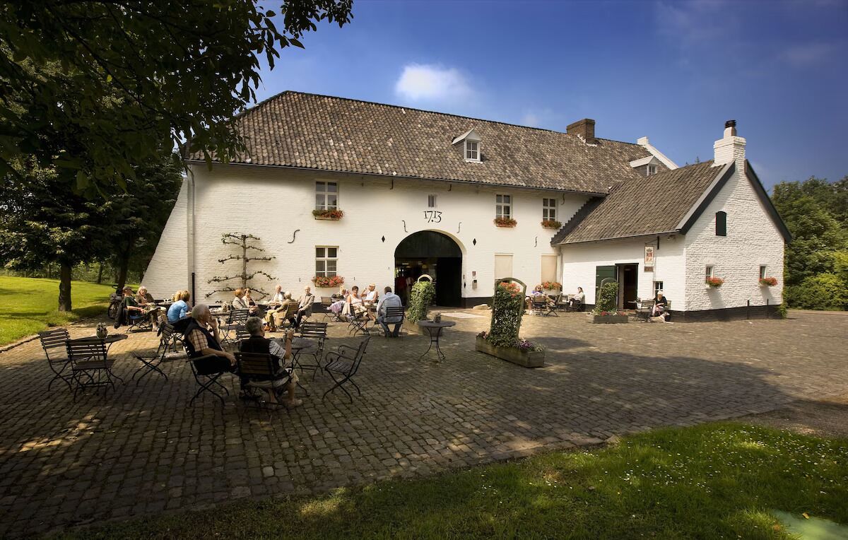 A white building with a tiled roof and a large arched entrance. There are outdoor seating areas with tables and chairs.
