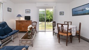 A living room with a sofa, coffee table, TV, wooden cabinet, and a dining area with chairs and a table. - Renovated Apartment with Private Garden, 150m from Saint-Colomban Beach (Carnac)