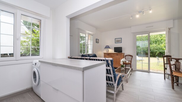 A modern kitchen with a built-in washing machine, a dining area with wooden chairs, and a large sliding glass door leading to an outdoor space. - Renovated Apartment with Private Garden, 150m from Saint-Colomban Beach (Carnac)