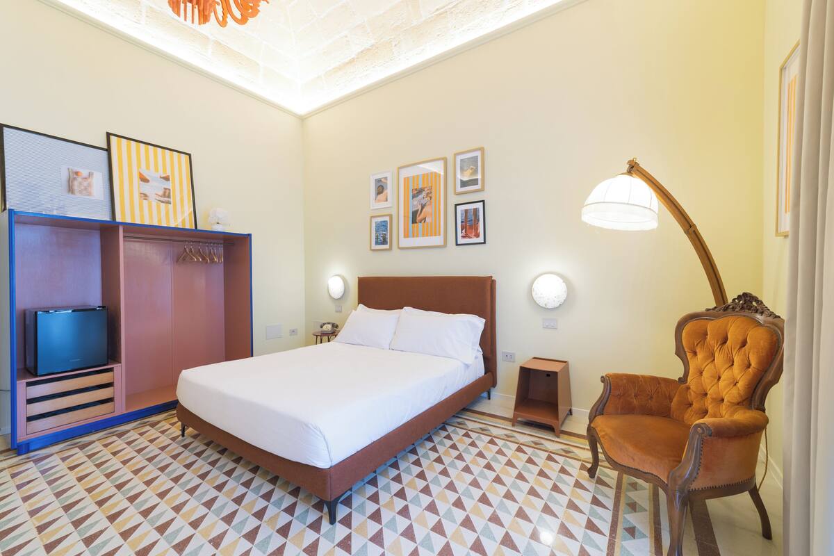 Ein Hotelzimmer mit Bett, Kleiderschrank, Sessel und Bildern an den Wänden.