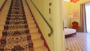 Una scala con tappeti decorati, una ringhiera rossa e un lampadario nella stanza adiacente.